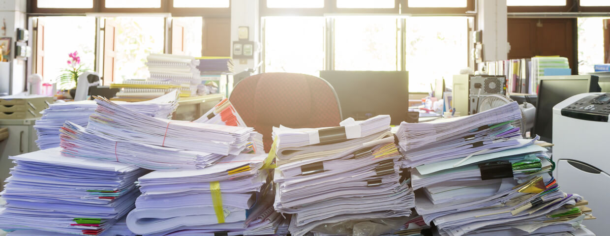 Stacks of paper on an office desk, in an office space.