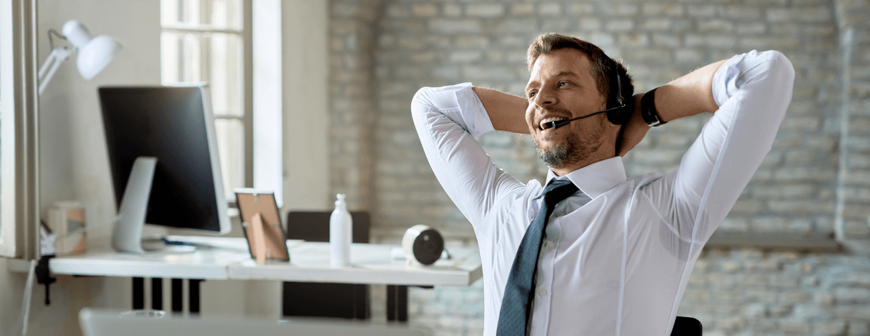 Business man stretching while using headset to speak on phone, in office setting.