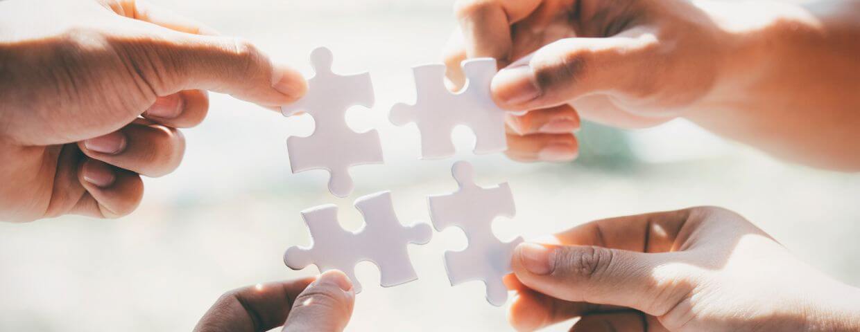 four hands bringing together puzzle pieces